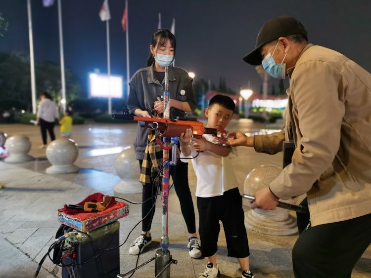 广场边上,2毛钱一枪的激光打气球小摊格外吸人眼球,一个小男孩举着