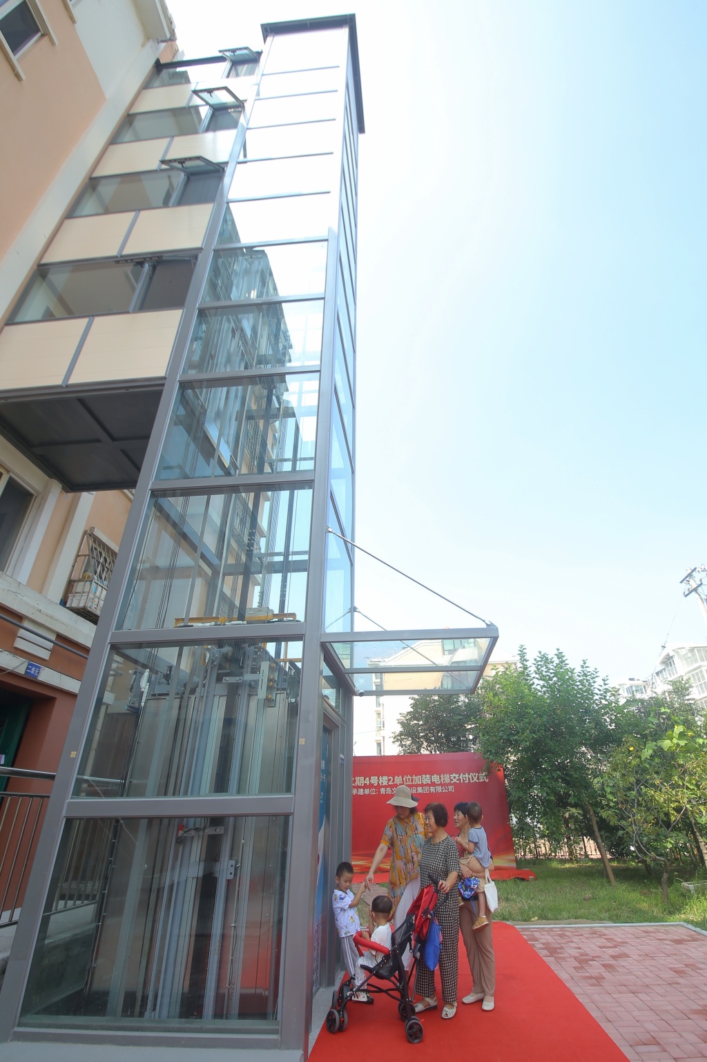 加装电梯采用钢结构框架,四周为彩钢板加透明玻璃幕墙围挡,兼顾外表