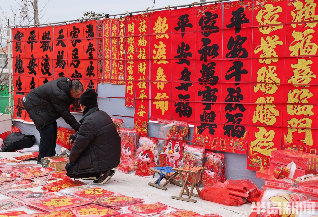半岛网>青岛>福字摊位上,摊主忙着为顾客挑选福字,对联各种熟食福字